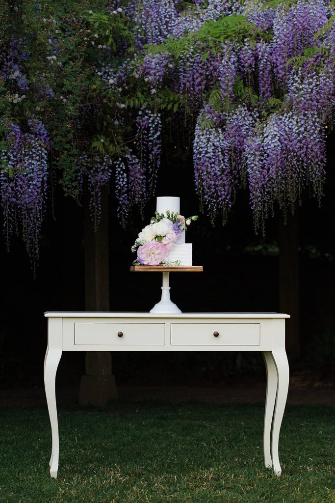 wedding cake sitting on trestle table with wisteria behind cake